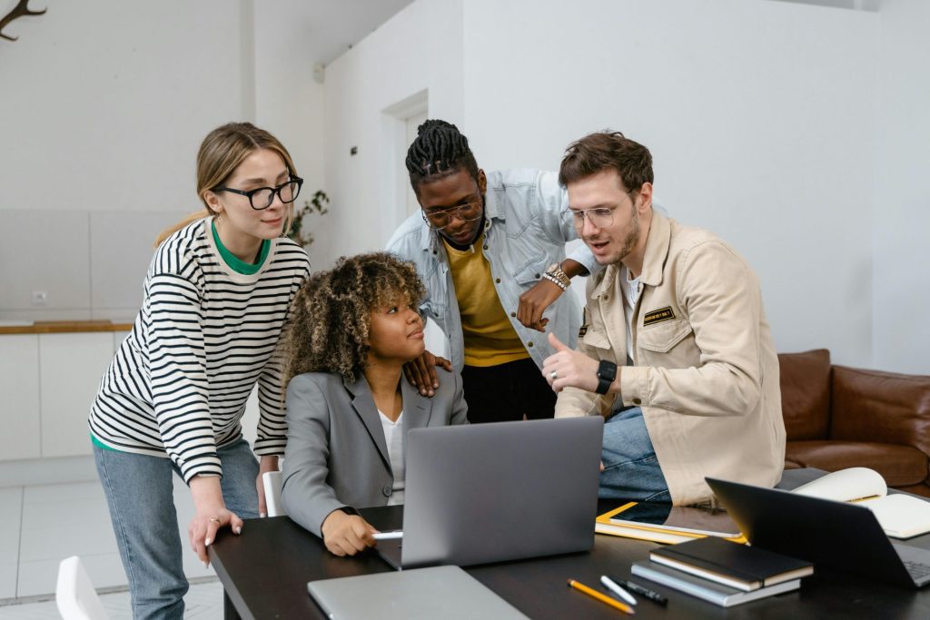 A dynamic group of four diverse adults collaborating on a project with a laptop in an office setting.