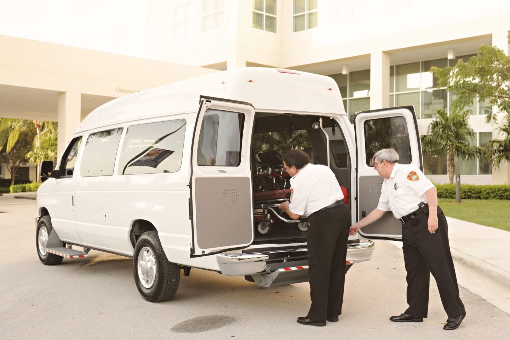 Two emergency responders load a stretcher into an ambulance outside a medical facility.